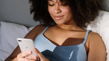 sexting / meisje ligt met haar telefoon in bed foto's verwijderen telefoon app